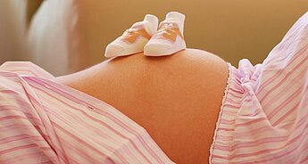 A pregnant woman's belly is adorned with a pair of baby shoes.