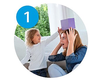 A child places a purple box on a woman's head.