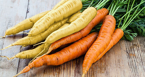 Carrots with green tops laid on a wooden surface.