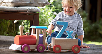 A child interacts with a wooden toy train on a deck.
