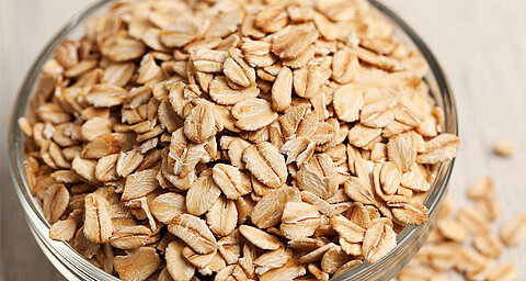 A transparent bowl filled with oat flakes.