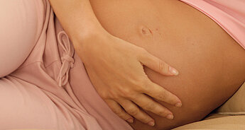 A pregnant woman in pink clothing, resting her hand on her belly.