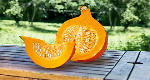 A sliced pumpkin rests on a wooden surface with a blurred garden background.