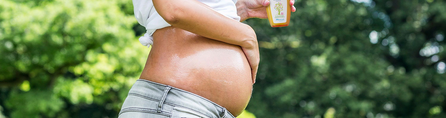 A person is applying sunscreen to their abdomen while standing outdoors.