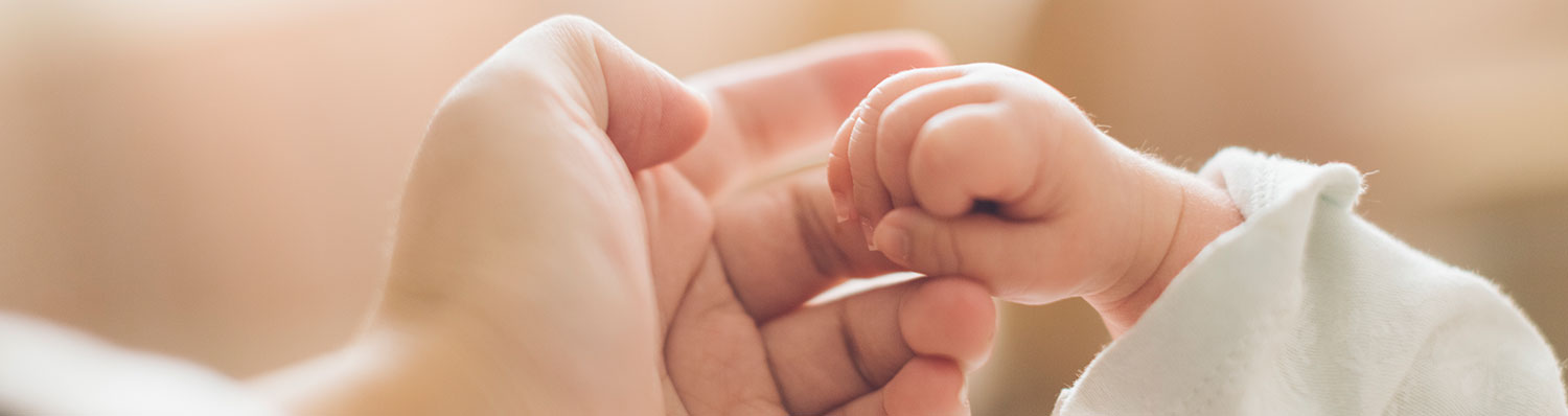 Two hands, one adult and one baby, are gently holding each other.