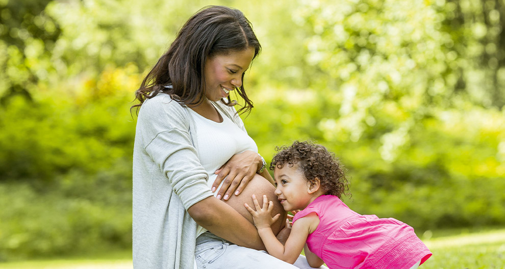 A pregnant woman and a young child outdoors.