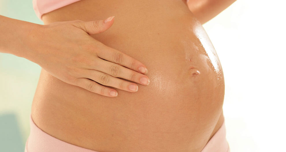 A pregnant woman in pink clothing, with her hand placed on her belly.