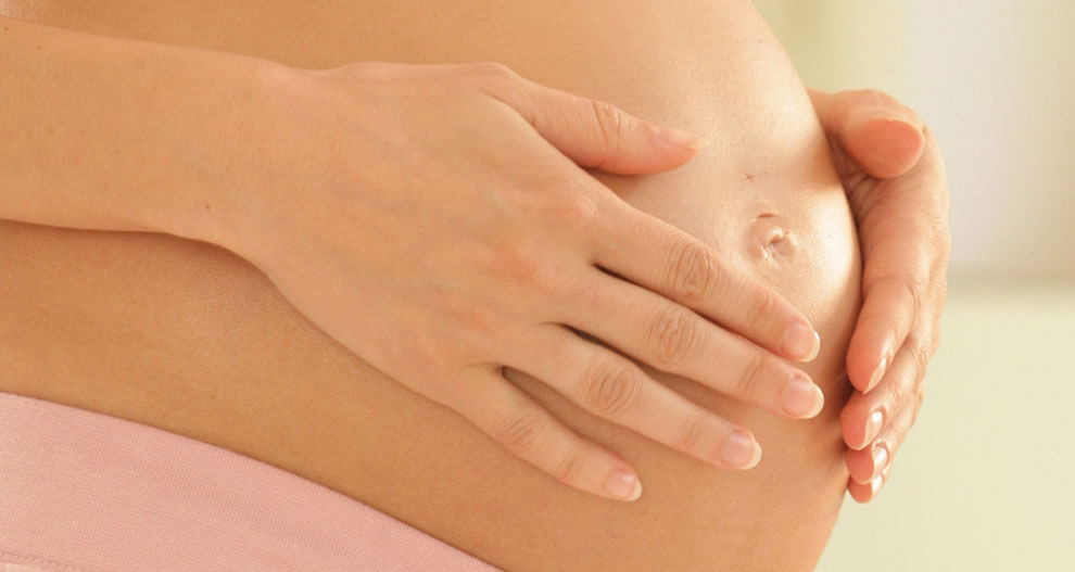 A pregnant woman's hands gently resting on her belly.
