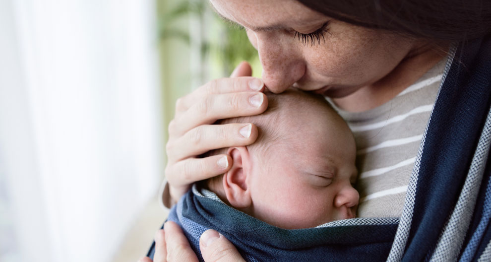 A woman is holding a baby close to her, with the baby's head resting on the woman's chest.