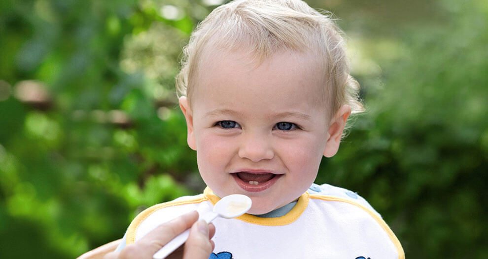 A young child with a spoon is being fed.