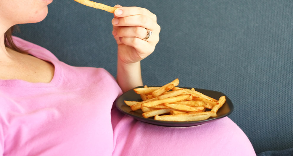 A woman in a pink shirt is eating fries from a black plate.