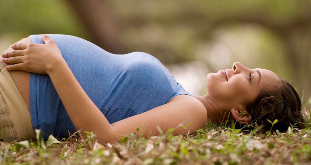 A pregnant woman lies on grass, looking up, with her hand on her belly.