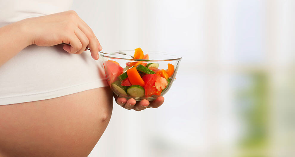 A pregnant woman eating a salad.