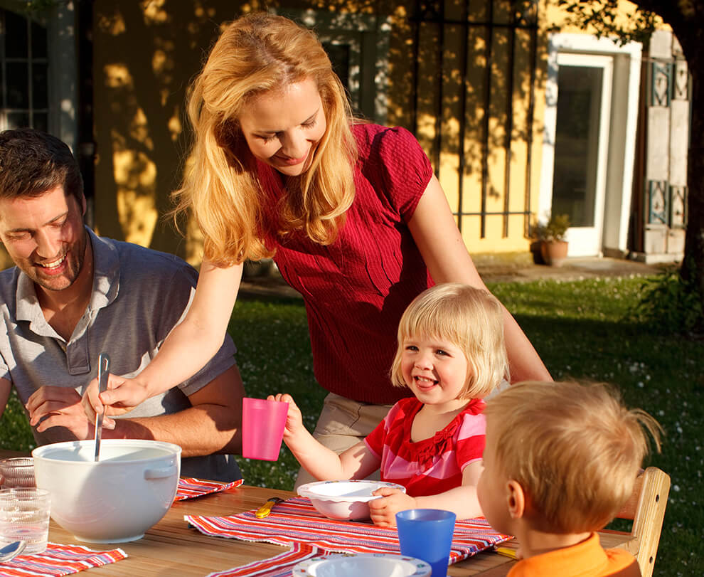 A family of four is seated at an outdoor table, engaged in a mealtime activity.