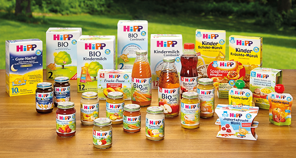 Various Hipp baby food products displayed on a table with a green outdoor background.